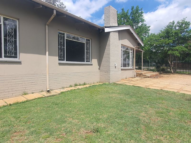 Rear view of the property featuring a brick chimney, paved patio area, and a lawn with perimeter fencing.