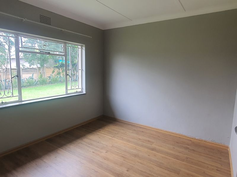 A vacant bedroom featuring laminate flooring, neutral wall paint, and a large window fitted with security bars.