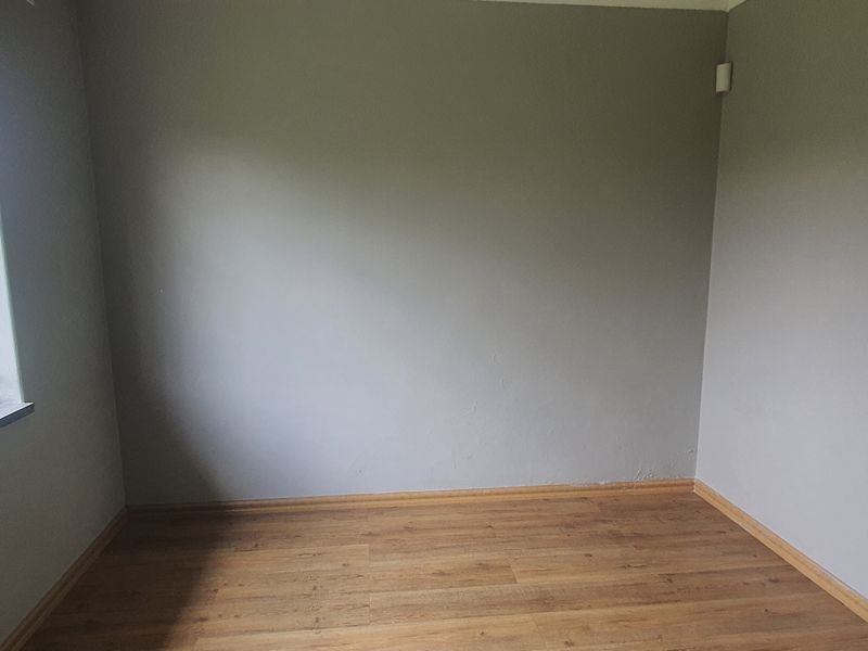 An empty bedroom featuring laminate flooring, neutral grey walls, and a window fitted with security bars.