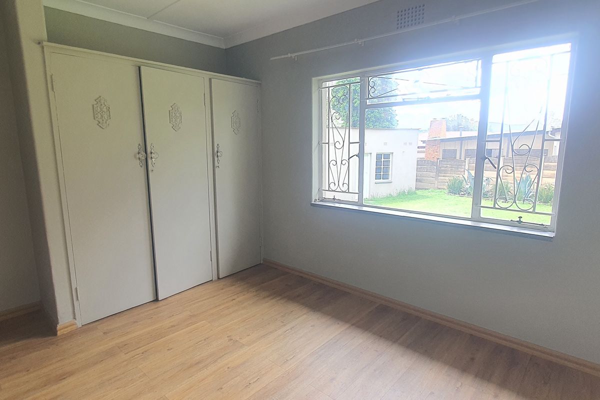 A bright, empty bedroom featuring laminate flooring, built-in cupboards, and security bars on the window overlooking the rear garden.