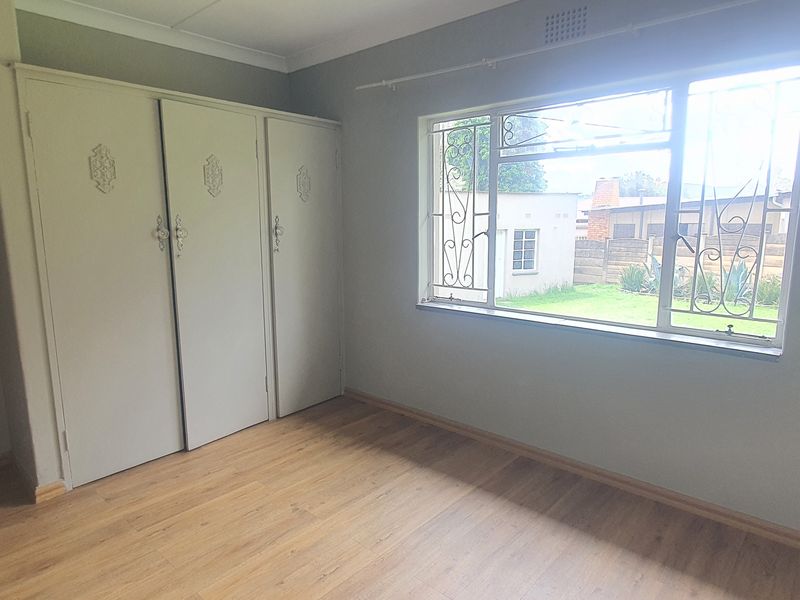 A bright, empty bedroom featuring laminate flooring, built-in cupboards, and security bars on the window overlooking the rear garden.