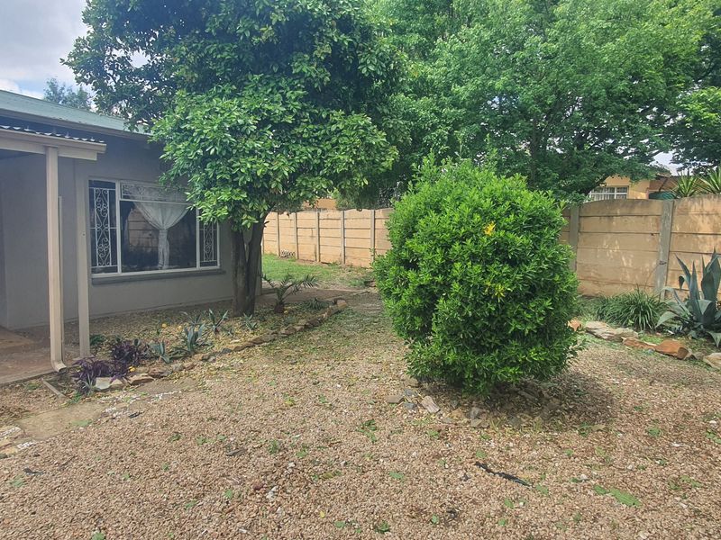 Rear view of the property featuring a covered patio area, established garden landscaping, and a secure precast concrete boundary wall.