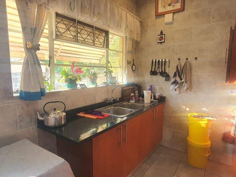 A functional kitchen featuring granite countertops, double basin sink, and tiled wall finishes with ample natural light from the window.