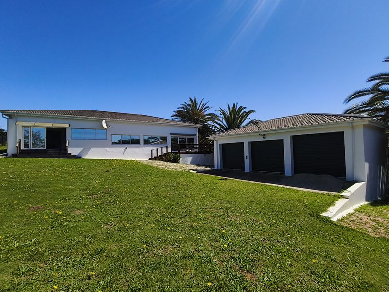 Rear view of the property featuring a spacious lawn, a triple garage, and a deck area with sliding door access to the main house.
