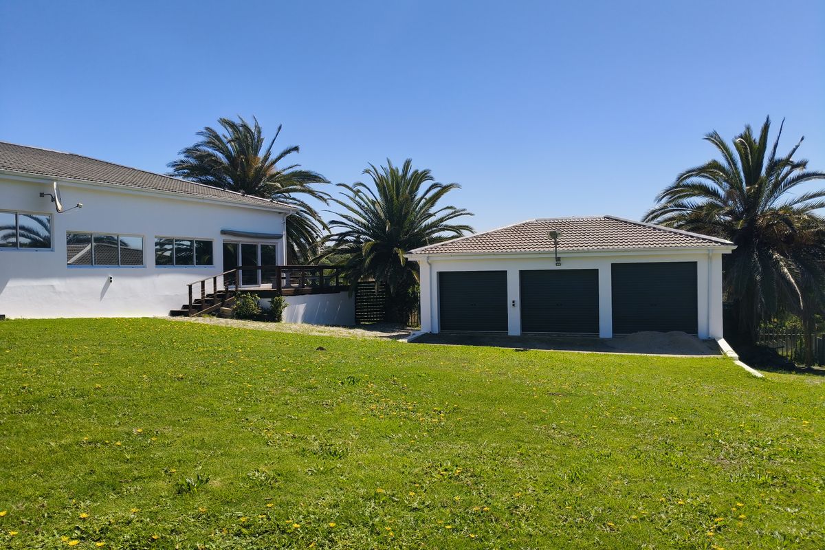 Rear view of the property featuring a spacious lawn, a triple garage, and a wooden deck leading to the main house.