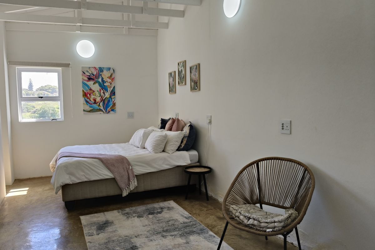 A bright bedroom featuring exposed timber rafters, polished concrete flooring, and wall-mounted lighting, offering a clean and modern aesthetic.