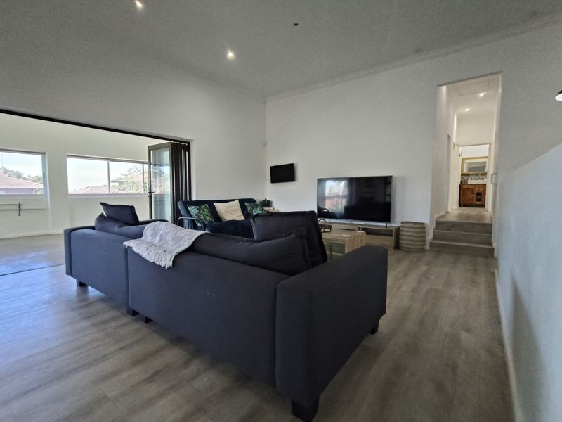 Spacious living room featuring modern laminate flooring, recessed downlights, and bi-fold doors leading to an outdoor area, with a staircase leading to the hallway.