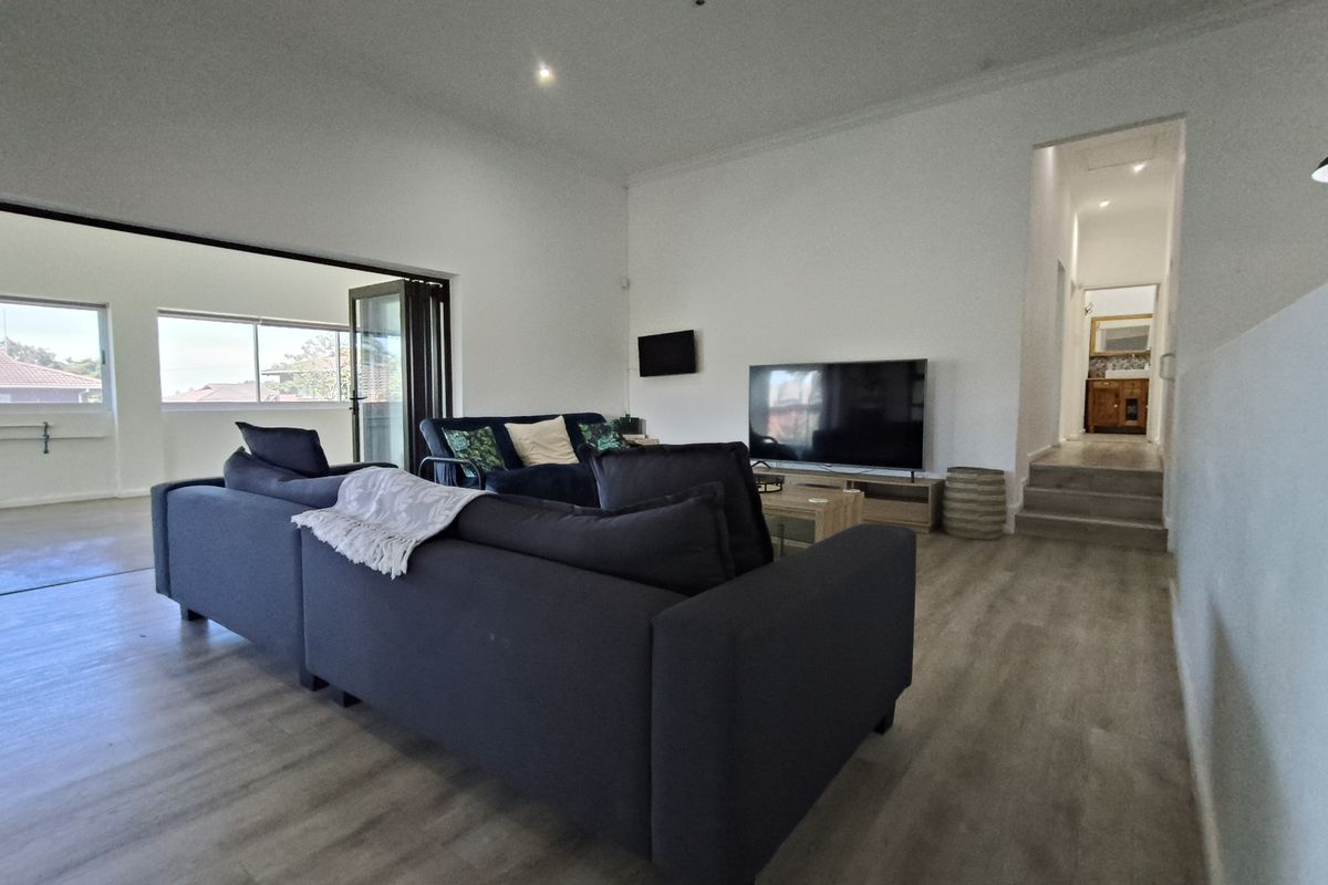 Spacious living room featuring modern laminate flooring, recessed downlights, and bi-fold doors leading to an outdoor area, with a staircase leading to the hallway.