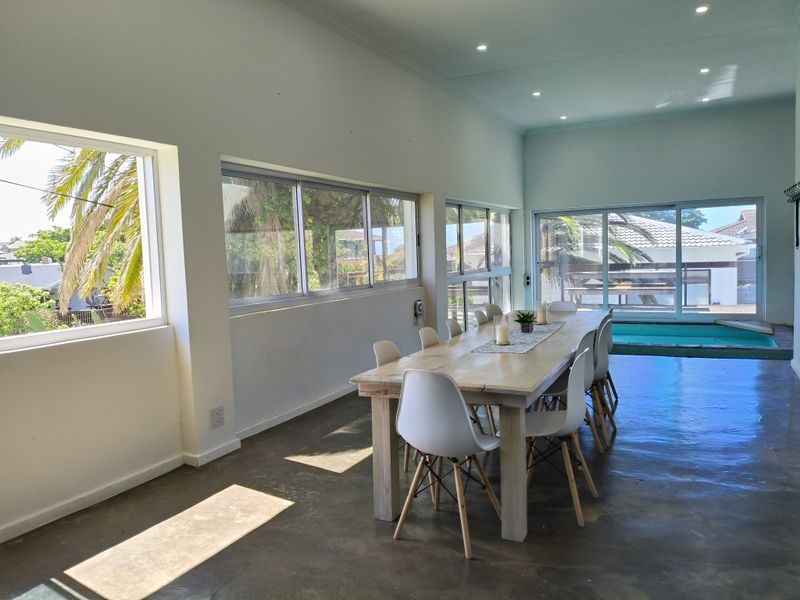 Spacious open-plan dining area featuring polished concrete floors, recessed lighting, and large windows providing natural light and views of the outdoor pool area.