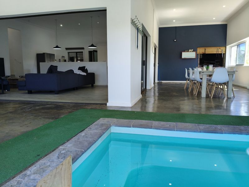 Open plan living and dining area featuring polished concrete floors, a built-in braai, and seamless flow to an outdoor swimming pool.