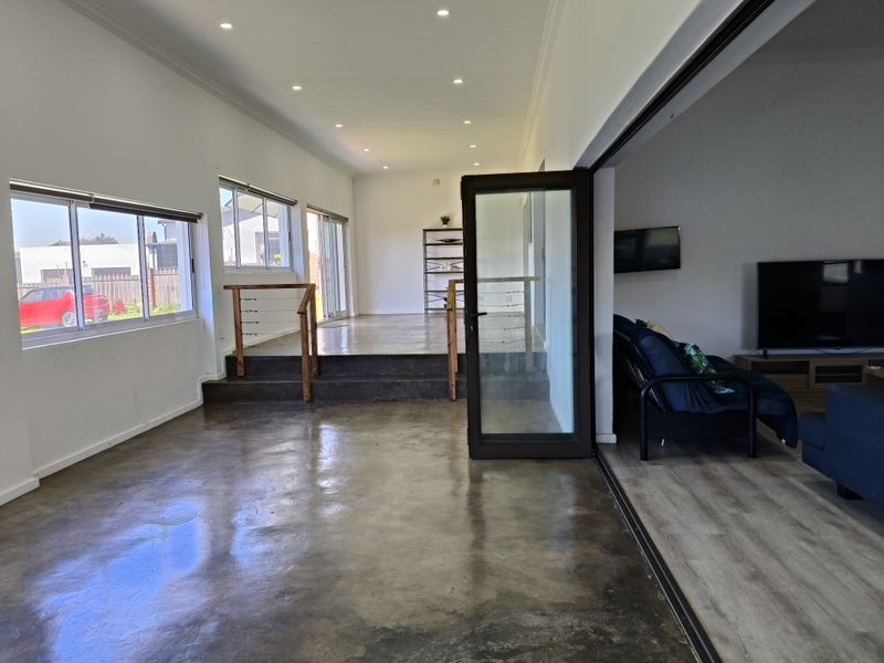 Spacious open-plan living area featuring polished concrete floors, recessed lighting, and a raised platform section with modern timber and cable balustrades.