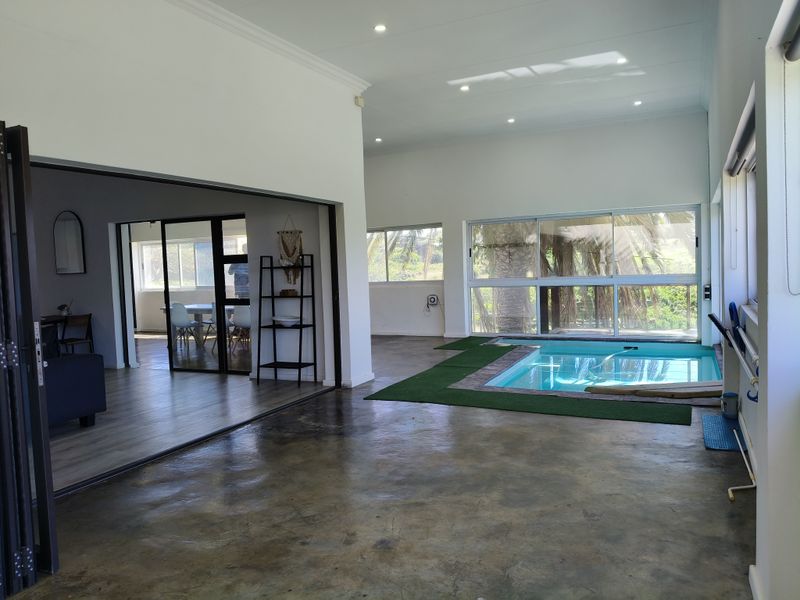 Spacious open-plan living area featuring a unique indoor swimming pool, polished concrete floors, and large sliding doors opening to the exterior.