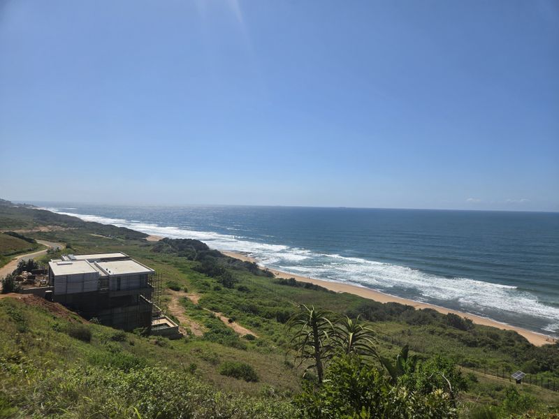 A scenic elevated view overlooking the coastline, sandy beach, and ocean, showcasing the property's prime coastal location.