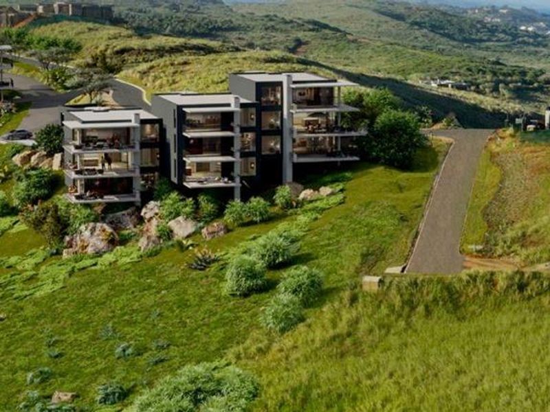 An aerial perspective of a modern residential development situated on a coastal hillside, showcasing the architectural layout and proximity to the ocean.