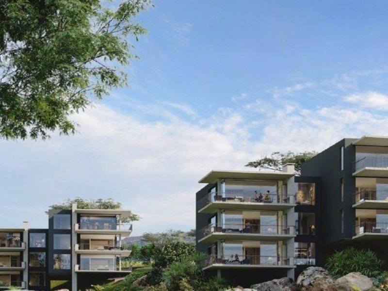 A modern apartment complex featuring multi-level units with expansive balconies and large glass facades set within a landscaped environment.