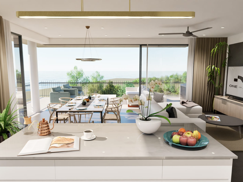 Modern open-plan living and dining area featuring a sleek kitchen island, recessed lighting, and expansive sliding doors opening to a balcony with ocean views.