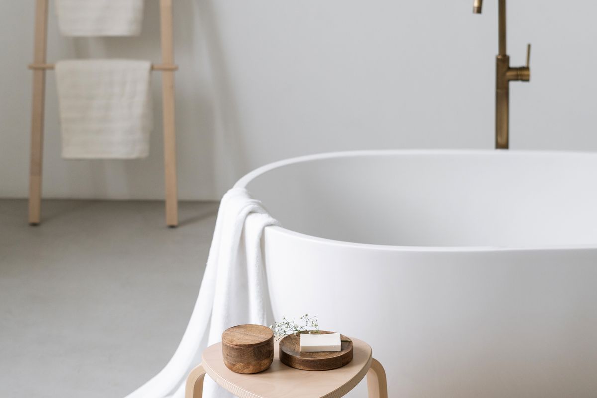 A modern bathroom featuring a minimalist freestanding bathtub paired with an elegant brass floor-mounted faucet.