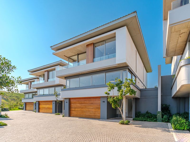 Modern multi-level townhouse exterior featuring timber garage doors, expansive glass windows, and paved driveway access in a contemporary residential estate.