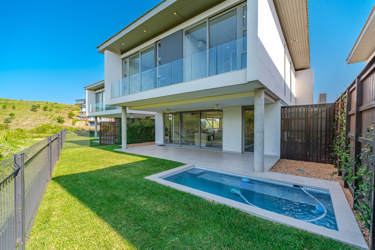 Modern townhouse rear exterior featuring a covered patio, private swimming pool, glass balustrades, and landscaped garden area.