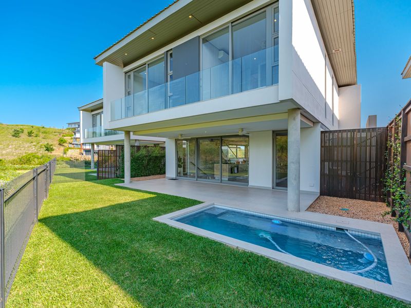 Modern townhouse rear exterior featuring a covered patio, private swimming pool, glass balustrades, and landscaped garden area.