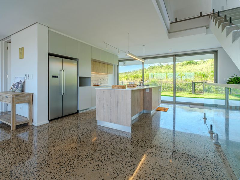 Modern open-plan kitchen and living area featuring polished concrete floors, a central island, and large glass sliding doors opening to the rear garden.