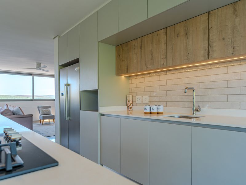 Modern open-plan kitchen featuring sleek cabinetry, stone countertops, subway tile backsplash, and integrated appliances, flowing seamlessly into the adjacent living area.
