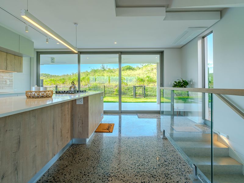 Modern open-plan kitchen featuring a central island, terrazzo flooring, and seamless indoor-outdoor flow through large sliding glass doors to the garden.