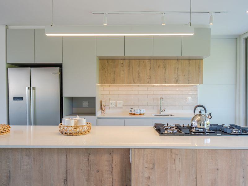 Modern kitchen featuring light wood-tone cabinetry, stone countertops, a gas cooktop, and a stylish subway tile backsplash with integrated lighting.