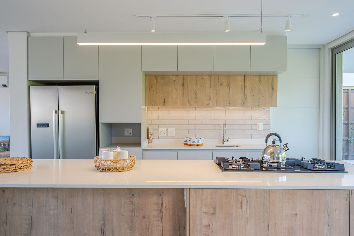 Modern kitchen featuring light wood-tone cabinetry, stone countertops, a gas cooktop, and a stylish subway tile backsplash with integrated lighting.