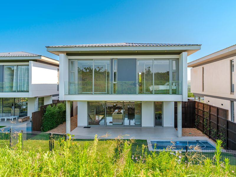 Rear view of a modern townhouse featuring a tiled patio, private swimming pool, glass balustrades, and large sliding doors opening to the living area.