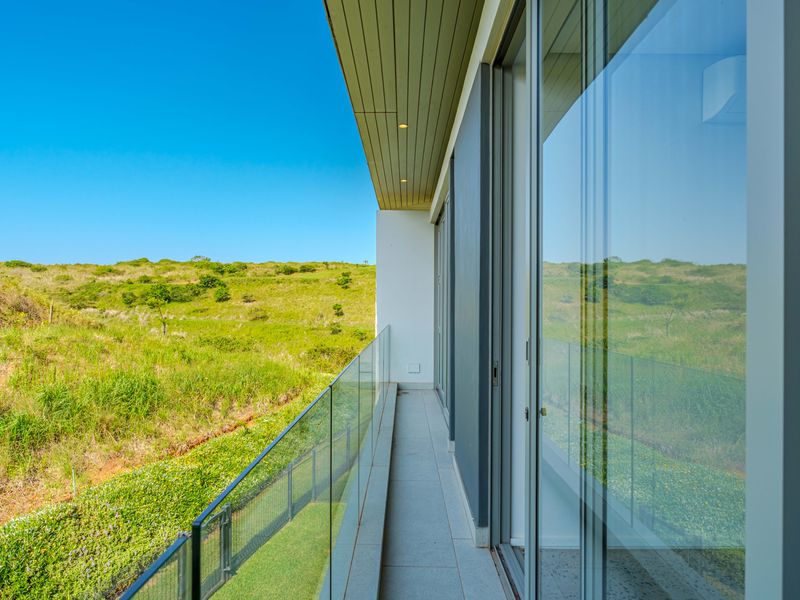 A modern balcony featuring a glass balustrade, tiled flooring, and sliding glass doors, offering expansive views of the surrounding natural landscape.