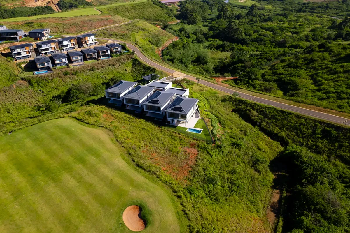 Aerial view of a modern residential estate featuring contemporary homes situated on a hillside overlooking a golf course and natural landscape.