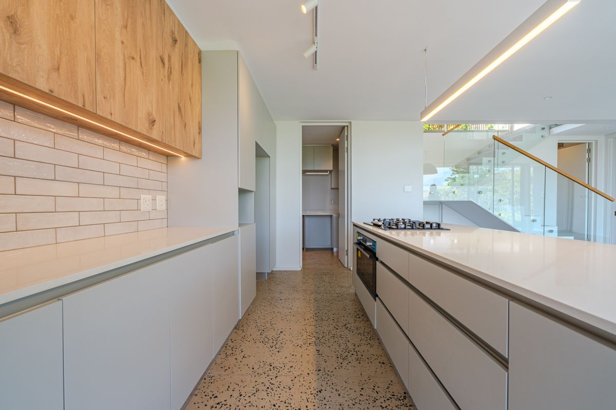 Modern kitchen featuring sleek handleless cabinetry, stone countertops, integrated gas hob, oven, and stylish terrazzo flooring with an adjacent scullery area.