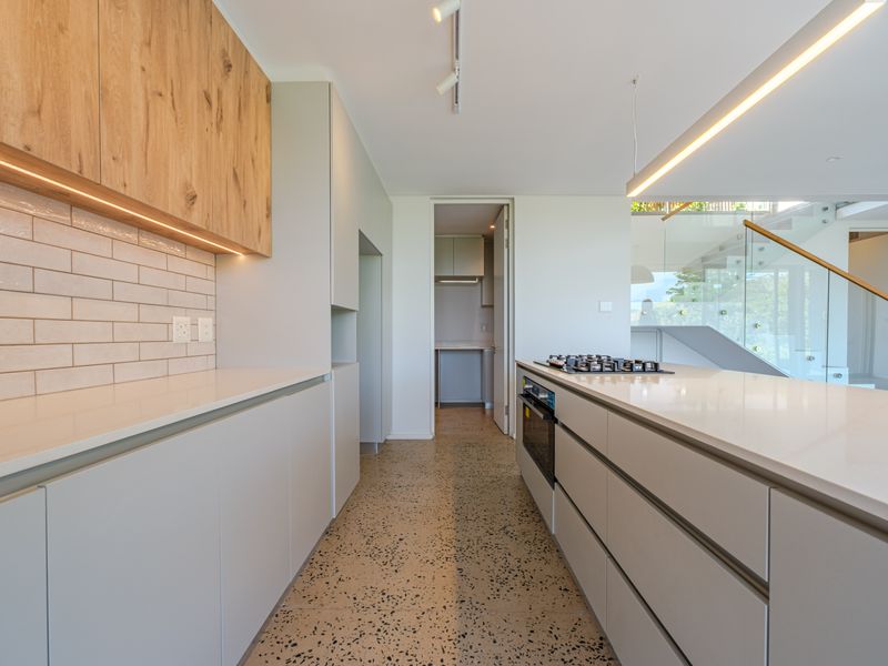 Modern kitchen featuring sleek handleless cabinetry, stone countertops, integrated gas hob, oven, and stylish terrazzo flooring with an adjacent scullery area.