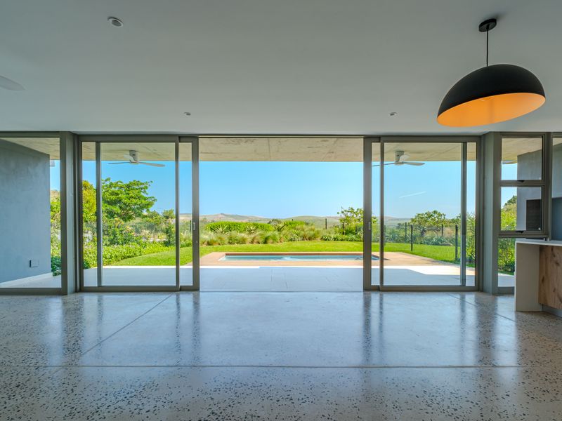 Spacious open-plan living area featuring polished concrete floors and large sliding glass doors that open onto a patio with a swimming pool and garden.