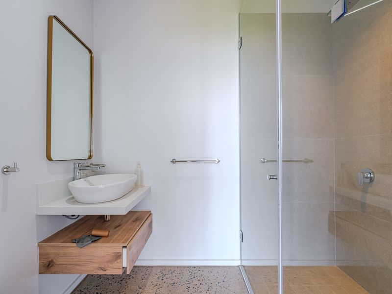 Modern bathroom featuring a floating wood vanity, vessel sink, glass-enclosed shower, and stylish terrazzo flooring with high-quality finishes.