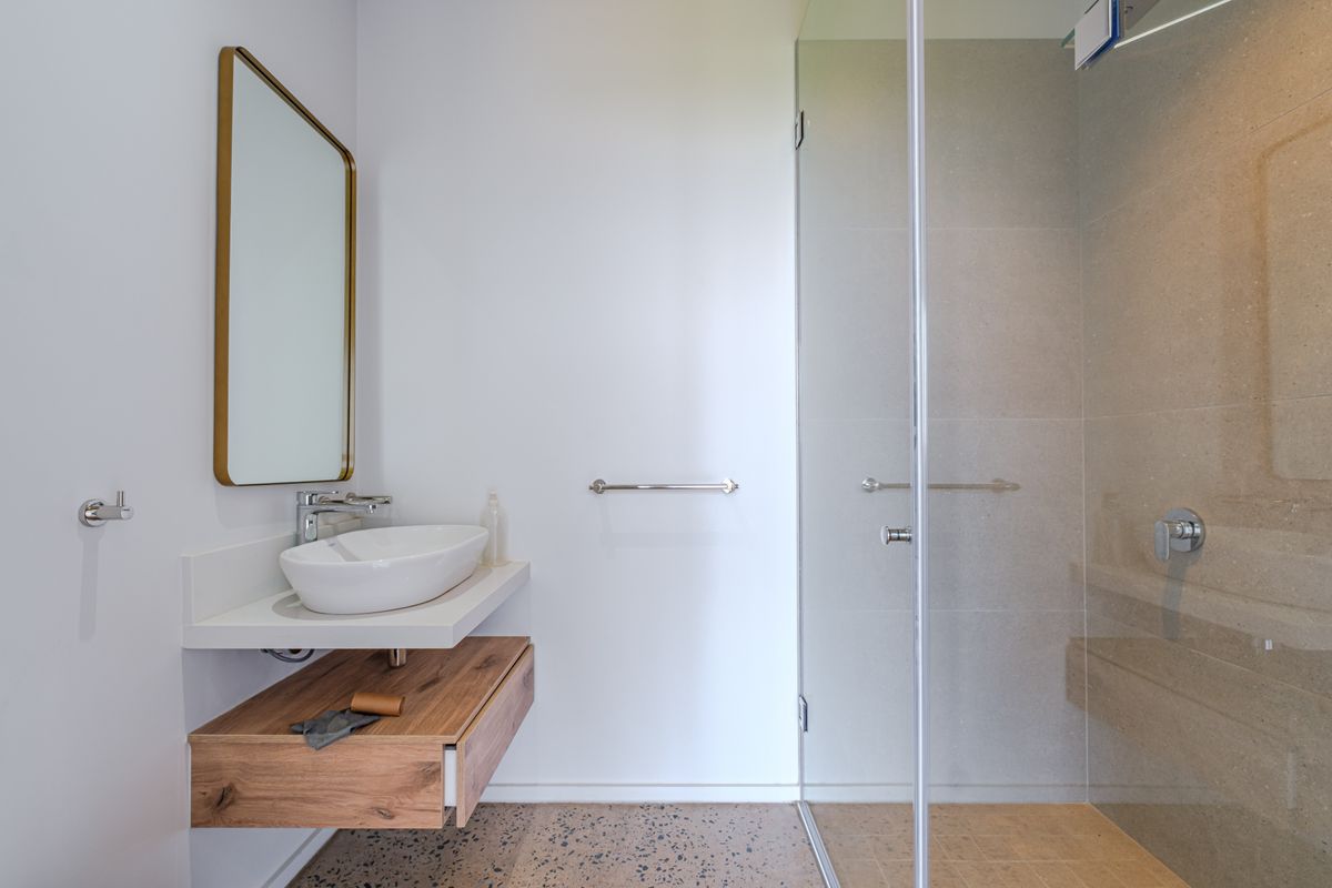 Modern bathroom featuring a floating wood vanity, vessel sink, glass-enclosed shower, and stylish terrazzo flooring with high-quality finishes.