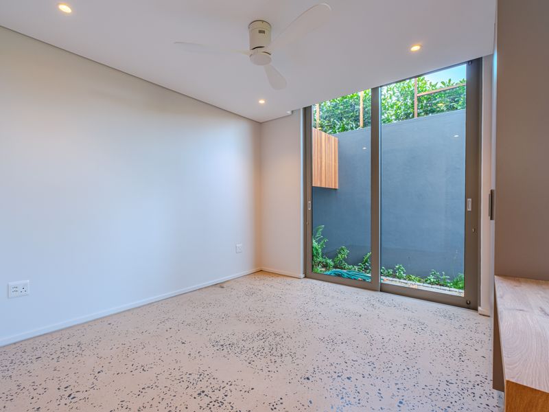 A bright, modern bedroom featuring terrazzo flooring, a ceiling fan, recessed lighting, and a large sliding glass door opening to a private courtyard.