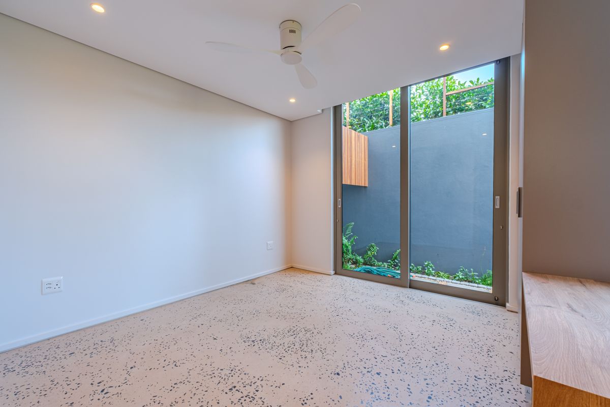 A bright, modern bedroom featuring terrazzo flooring, a ceiling fan, recessed lighting, and a large sliding glass door opening to a private courtyard.