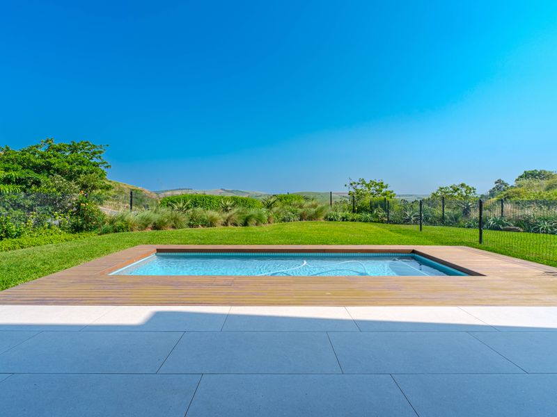 A well-maintained swimming pool featuring timber decking, surrounded by a landscaped garden and scenic hill views.