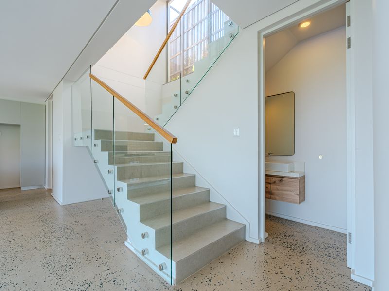 Modern hallway featuring a striking stone staircase with a glass balustrade, polished concrete floors, and access to a sleek powder room.