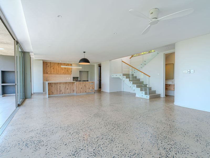 Spacious open-plan living area featuring polished terrazzo floors, a modern kitchen with wood-finish cabinetry, and a sleek staircase with glass balustrades.