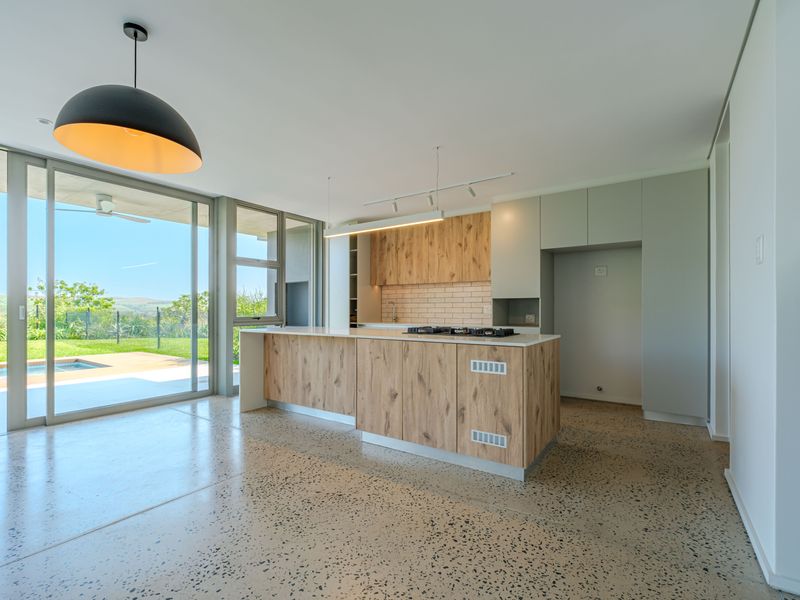 Modern open-plan kitchen featuring a central island with a gas hob, sleek cabinetry, and polished concrete floors, opening onto a patio and garden area.