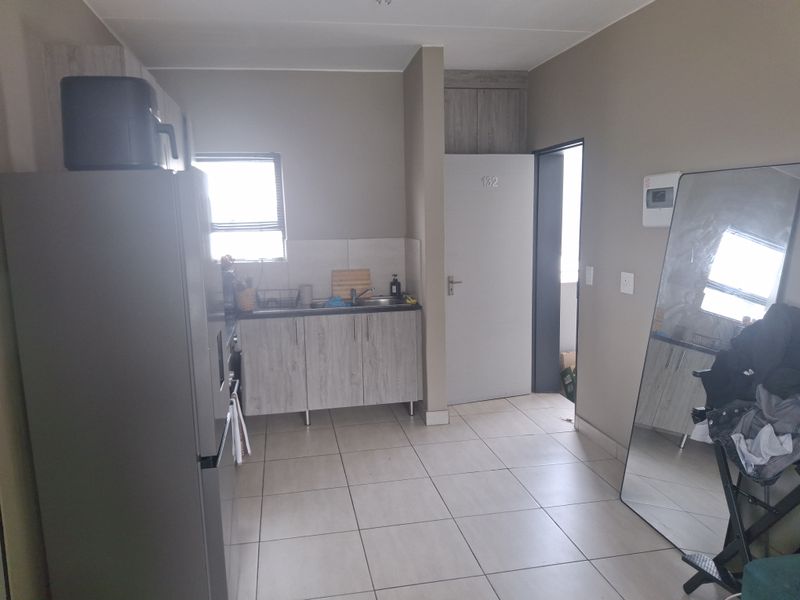 A functional kitchen area featuring built-in cabinetry, a stainless steel sink, tiled backsplash, and neutral floor tiles.