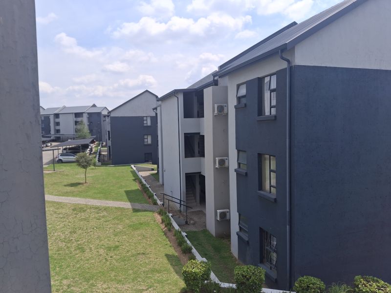 View of the apartment complex exterior featuring modern multi-story buildings, landscaped grounds, paved walkways, and installed air conditioning units.