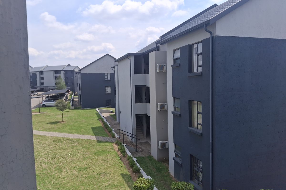 View of the apartment complex exterior featuring modern multi-story buildings, landscaped grounds, paved walkways, and installed air conditioning units.