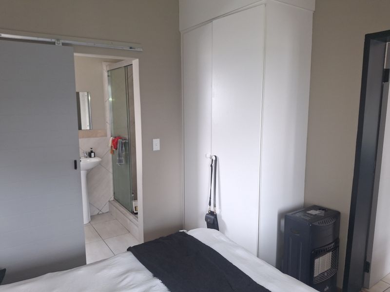 Bedroom featuring a built-in wardrobe and an adjoining en-suite bathroom with a shower and pedestal basin.