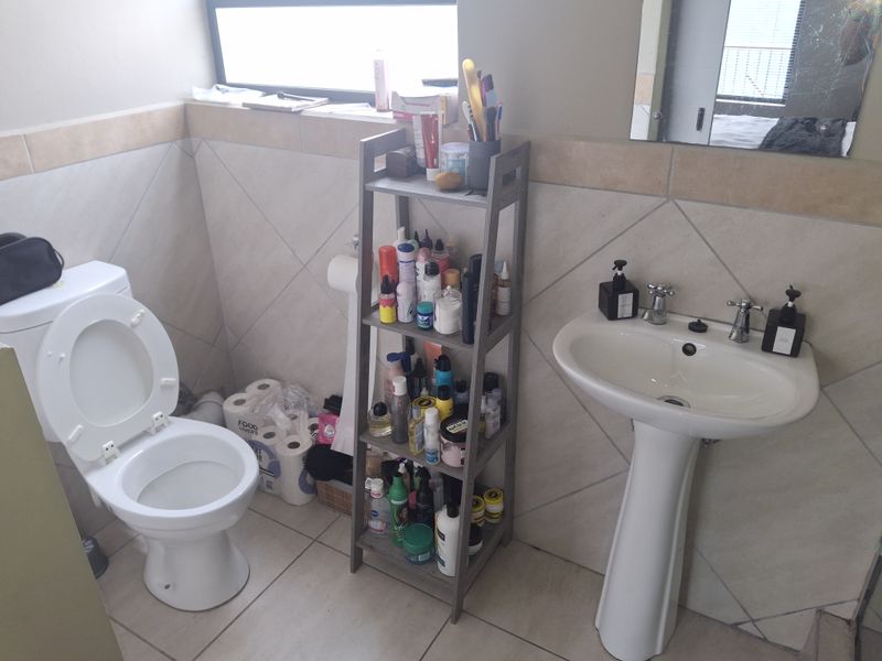 A functional bathroom featuring a pedestal basin, toilet, and neutral wall and floor tiling.