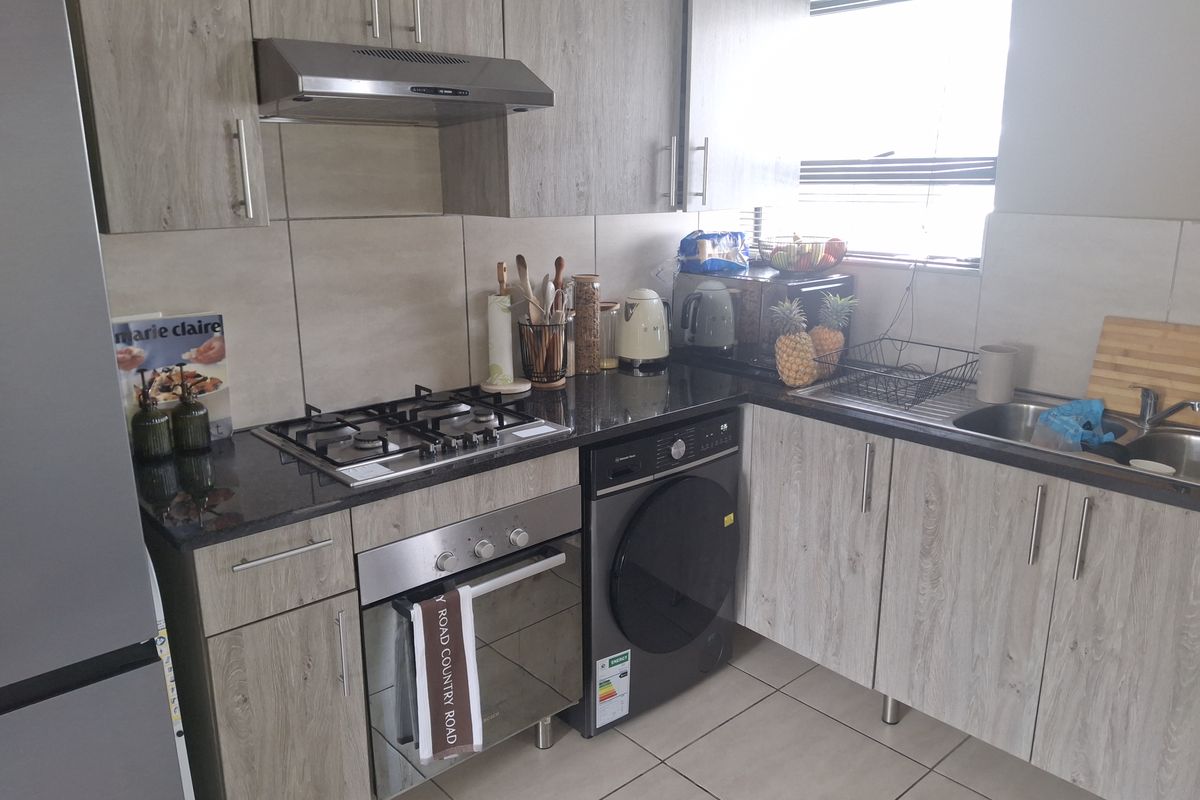 Modern kitchen featuring wood-look cabinetry, granite countertops, gas hob, built-in oven, extractor fan, and tiled finishes.