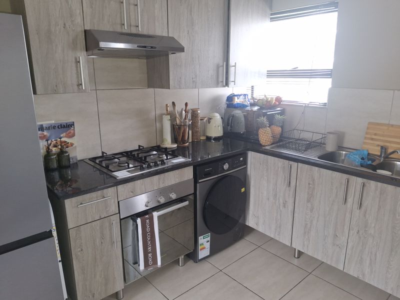 Modern kitchen featuring wood-look cabinetry, granite countertops, gas hob, built-in oven, extractor fan, and tiled finishes.